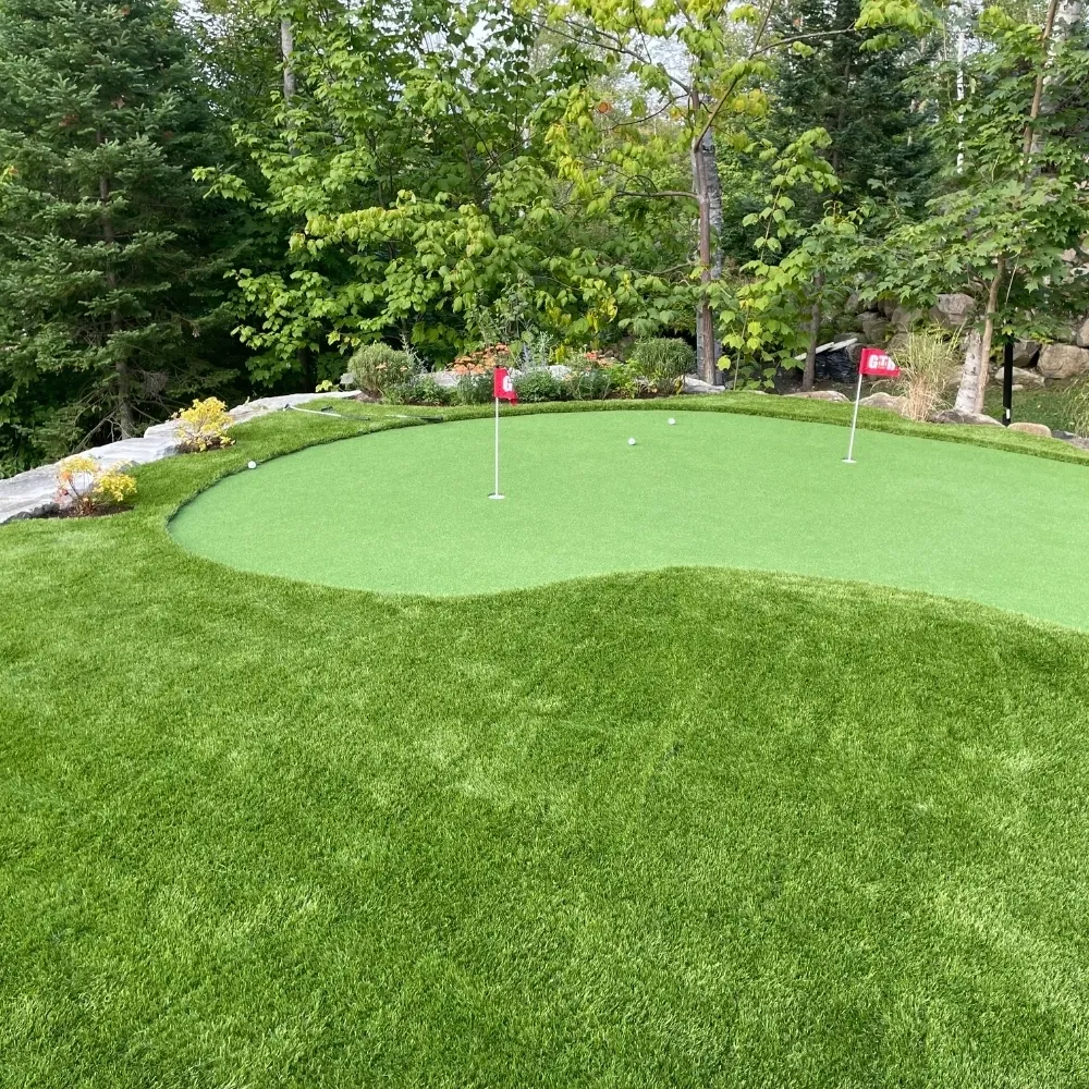 Backyard artificial grass putting green with golf holes and flags, surrounded by trees and landscaped garden.