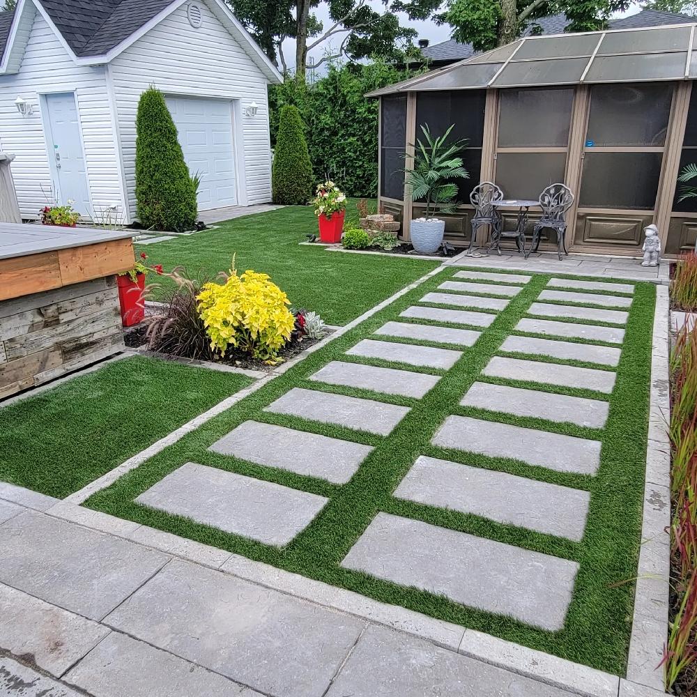 Residential backyard with artificial grass and concrete pavers pathway, landscaped plants, gazebo seating area, and a clean modern outdoor design.