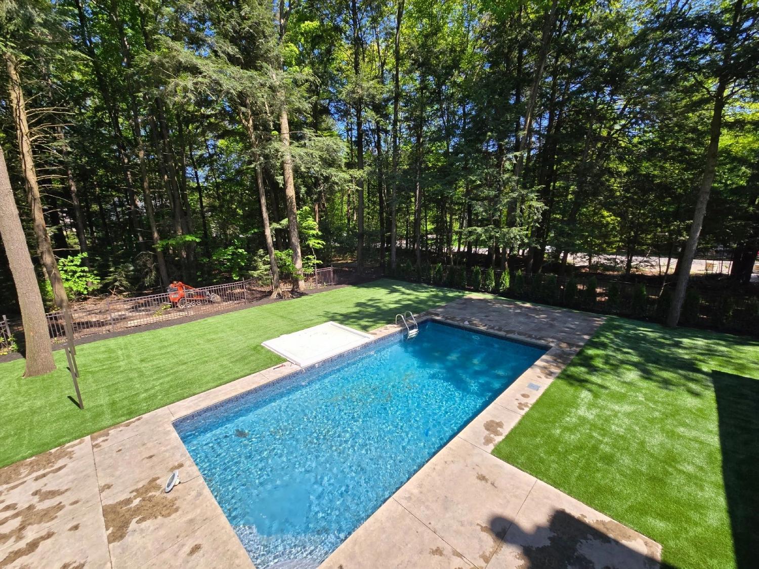 Backyard swimming pool surrounded by lush artificial grass landscaping and mature trees in a private residential outdoor space.