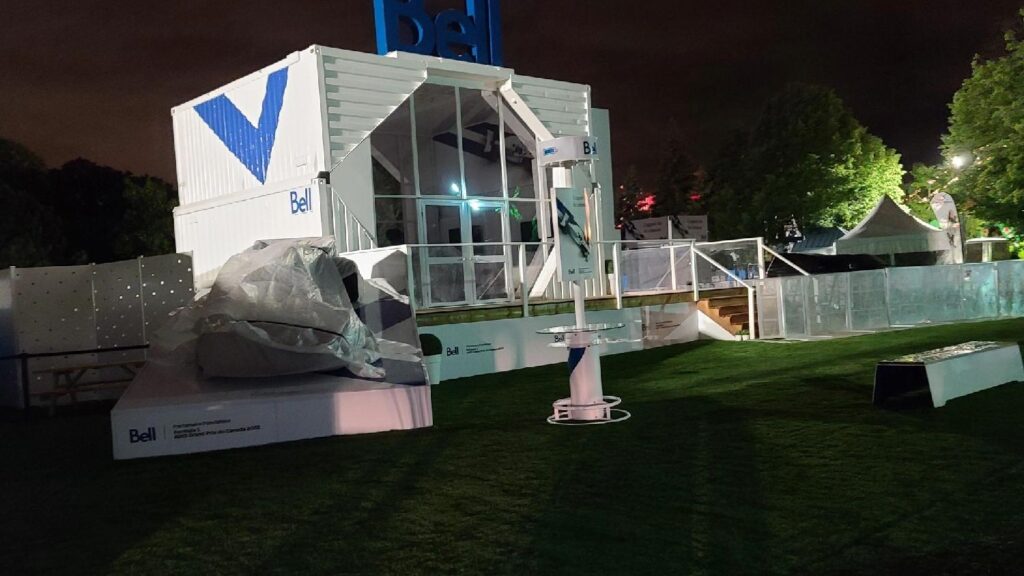 Nighttime branded event setup featuring a Bell activation booth, artificial turf flooring, modern display structures, and illuminated surroundings.