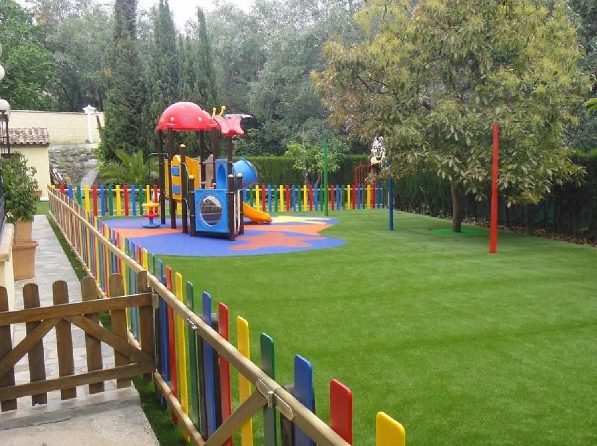 Secure children’s playground with artificial grass lawn, colorful fencing, play equipment, and safe family-friendly outdoor recreational space.