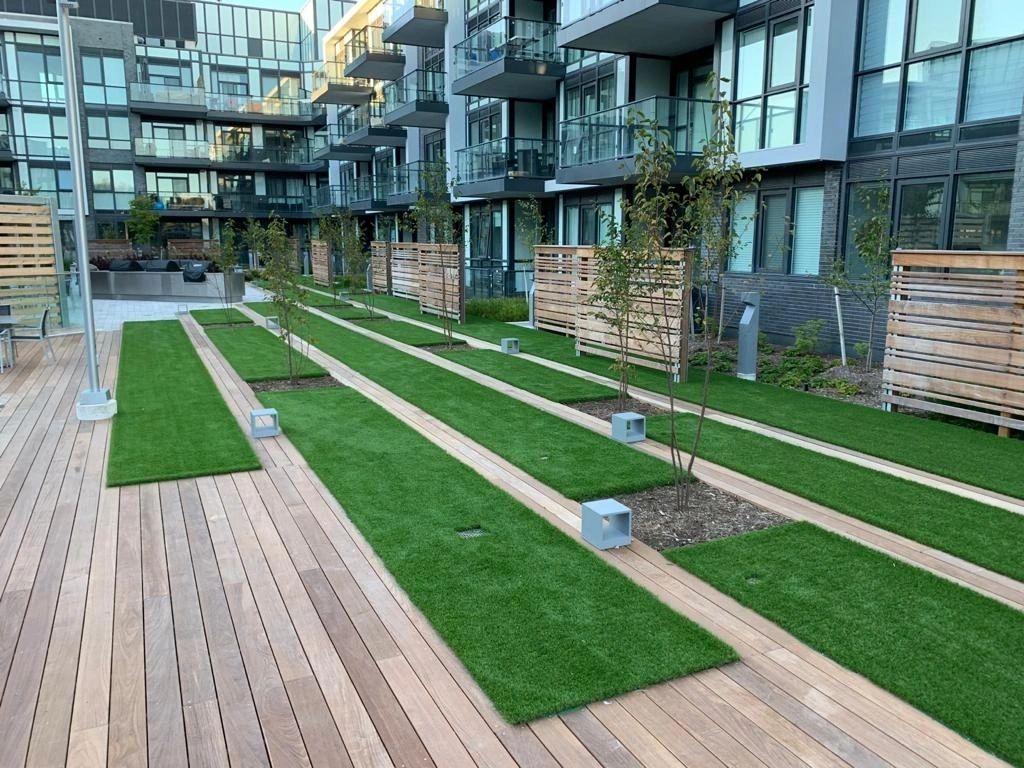 Modern apartment complex courtyard with artificial grass landscaping, wooden walkways, and contemporary outdoor communal living space.