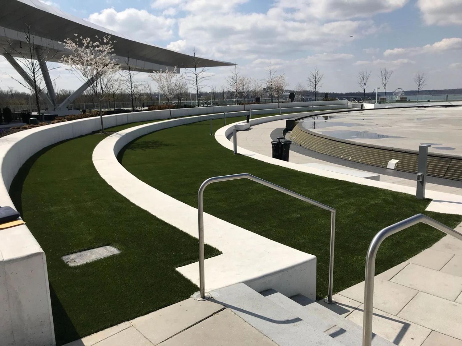 Modern commercial rooftop or terrace with artificial grass landscaping, curved architectural walkways, and premium outdoor public space design.