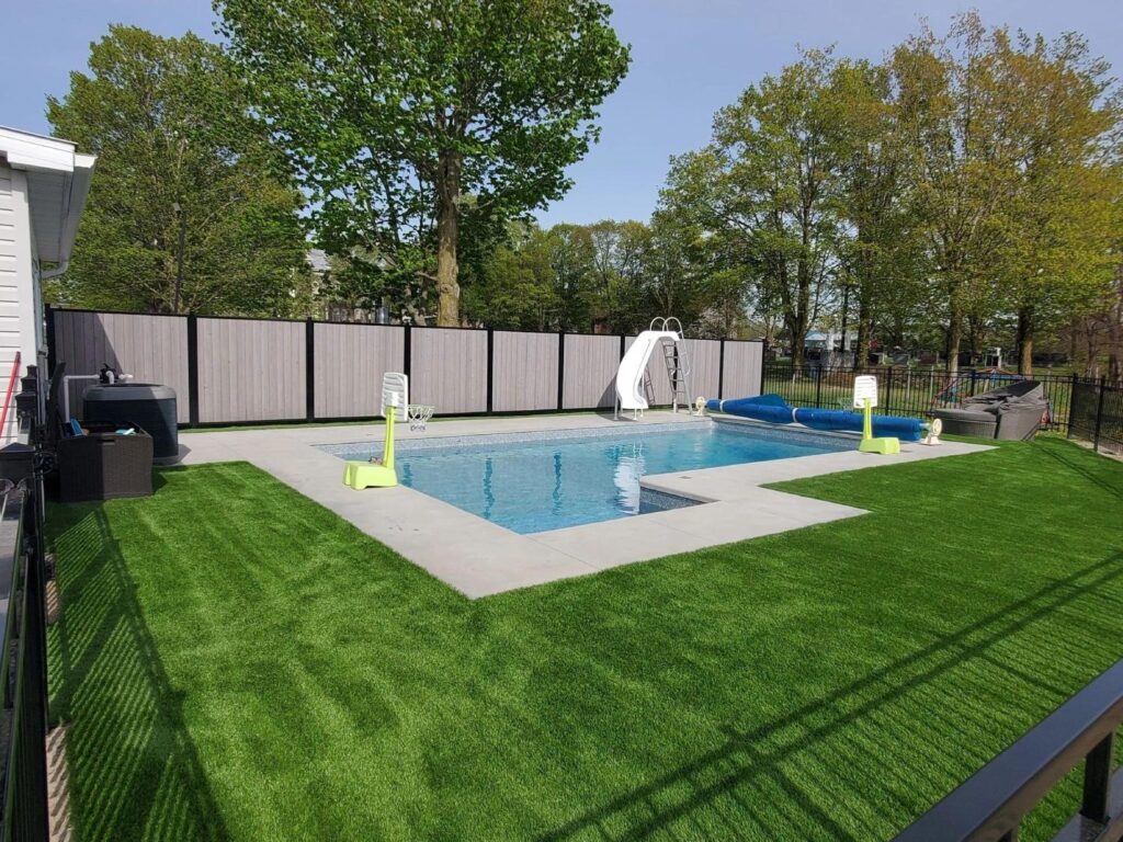Family backyard with swimming pool, artificial grass lawn, privacy fencing, and recreational outdoor space for children.