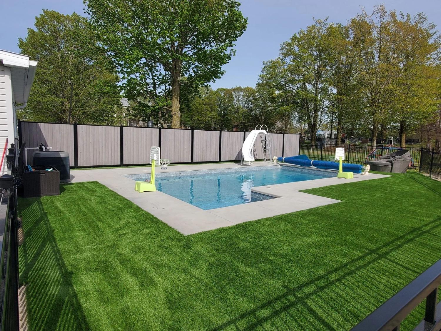 Family backyard with swimming pool, artificial grass lawn, privacy fencing, and recreational outdoor space for children.