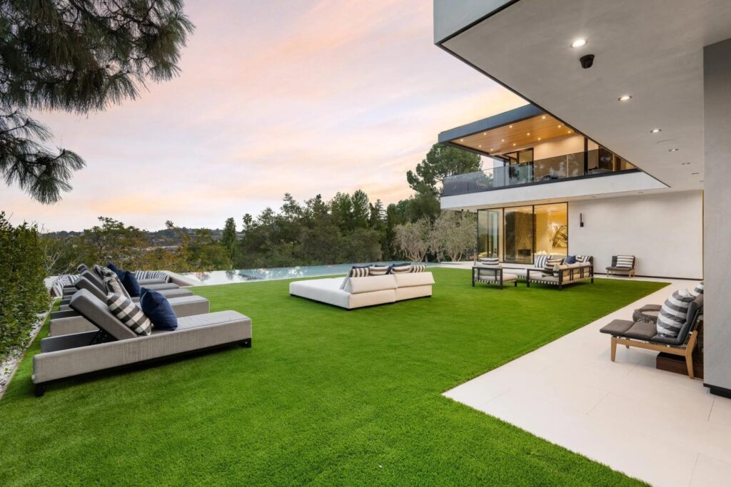 Modern luxury terrace with artificial grass lawn, outdoor lounge seating, and infinity pool overlooking scenic landscape at sunset.