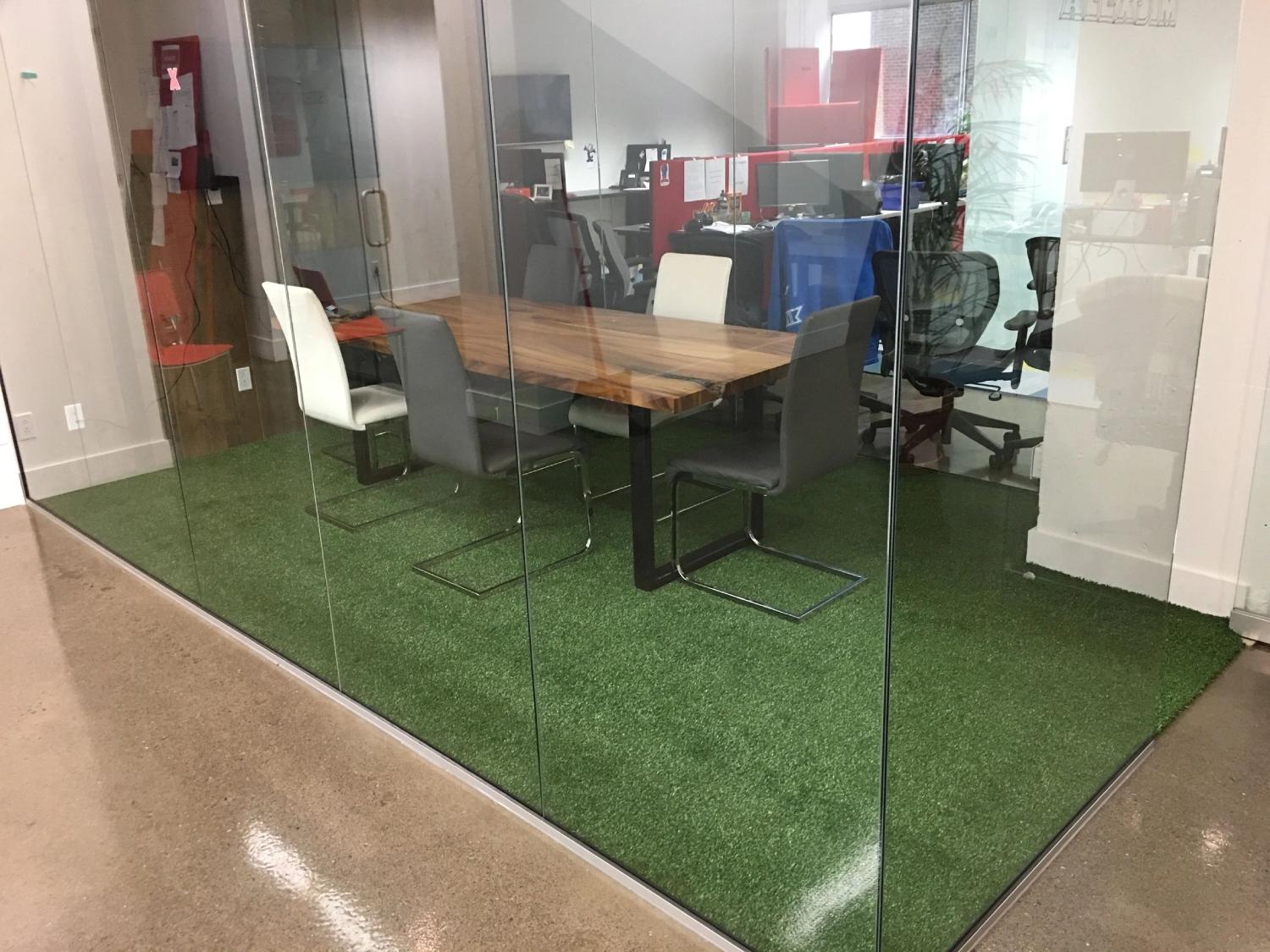 Modern office meeting room with artificial grass flooring, glass walls, conference table, and contemporary workspace design.