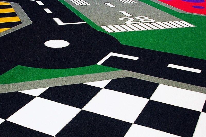 Artificial turf playground featuring a colorful road track design with roundabout markings, pedestrian crossings, and checkered patterns for interactive play.