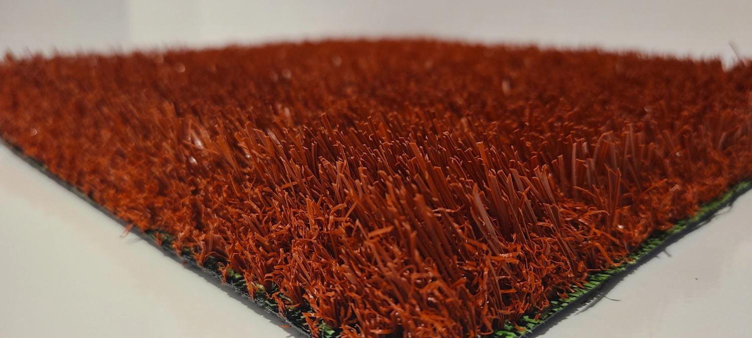 Close-up view of red artificial grass showing dense synthetic fibers and textured surface, commonly used for sports fields or decorative applications.