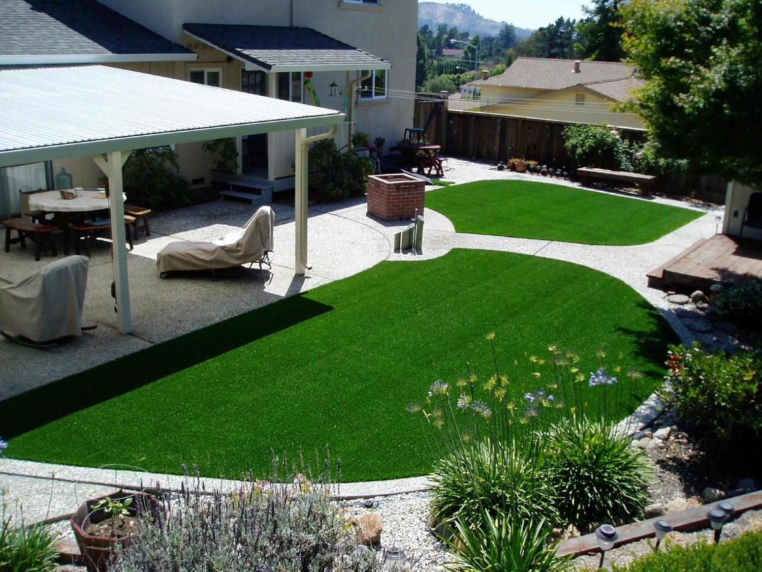 Residential backyard with custom artificial grass landscape design, covered patio, decorative walkways, and low-maintenance outdoor living area.