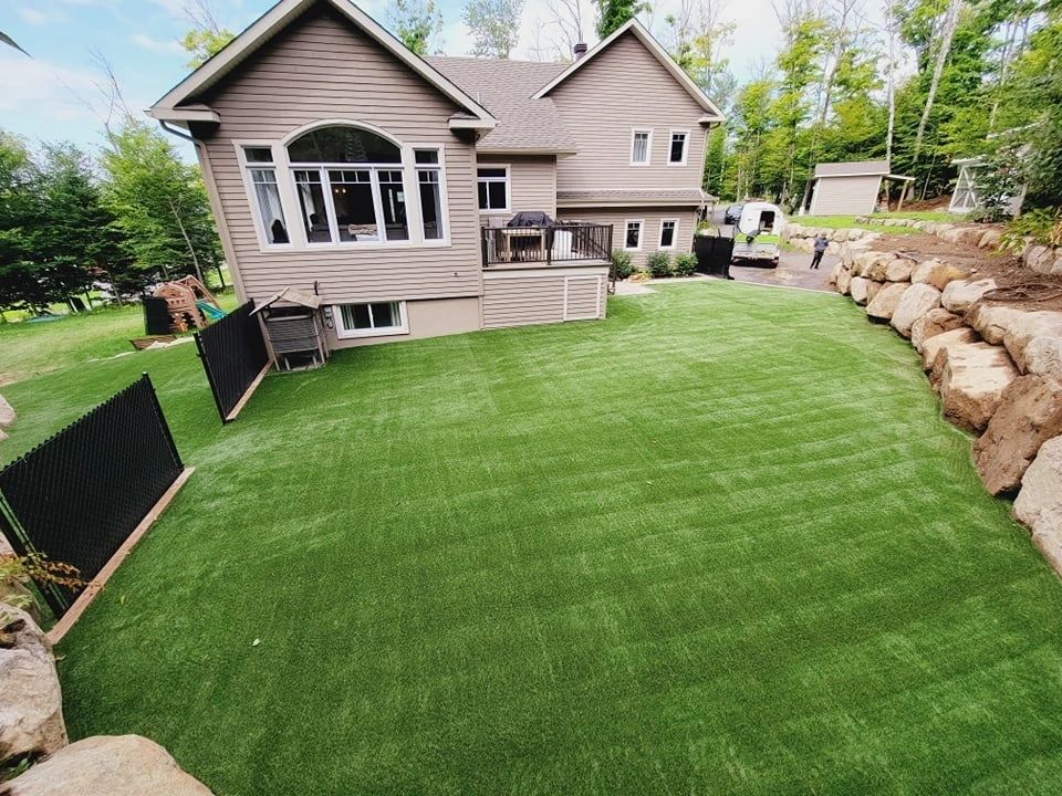 Modern home backyard with artificial grass lawn, landscaped stone retaining wall, and surrounding trees creating a clean and low-maintenance outdoor space.