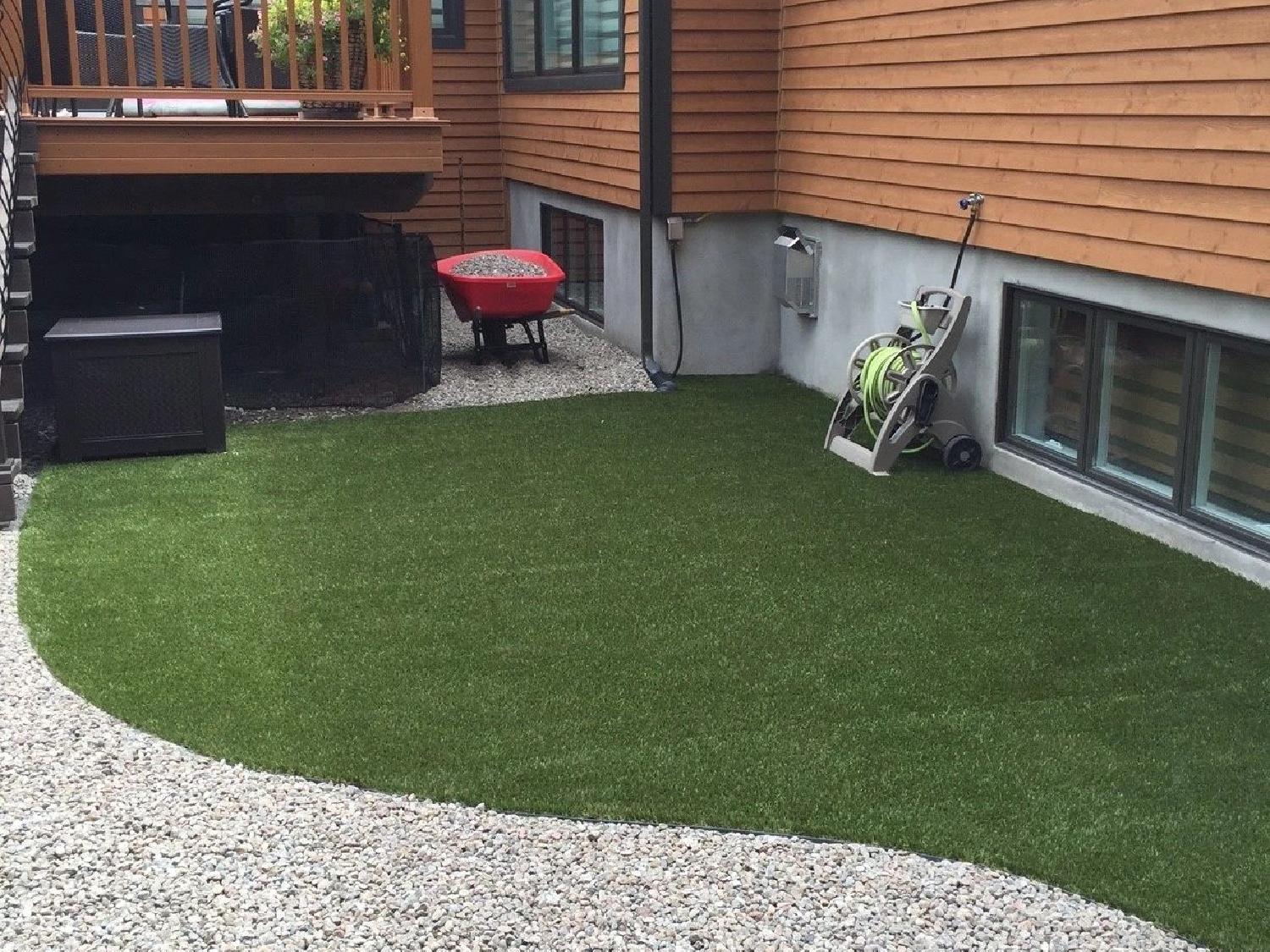 Small residential backyard with artificial grass lawn, gravel landscaping, and modern home exterior for low-maintenance outdoor living